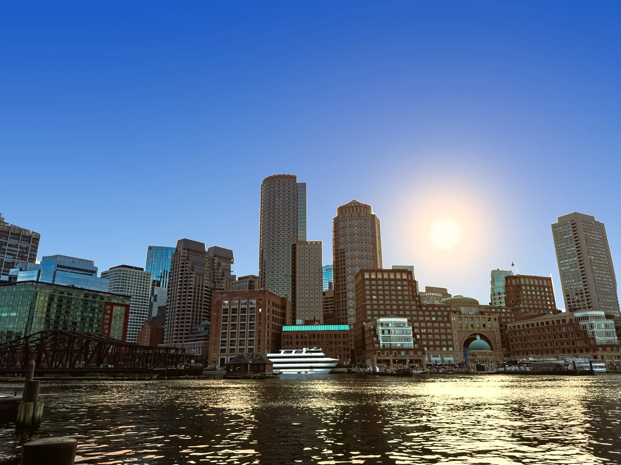 Boston harbor skyline under a clear sky with the sun shining